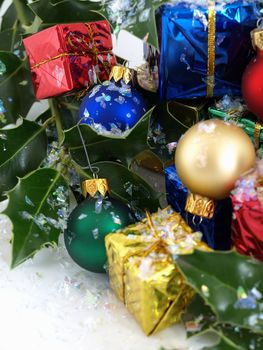 Colorful gift boxes, Christmas bulbs and holly, sprinkled with artificial snow. Isolated on a white background.