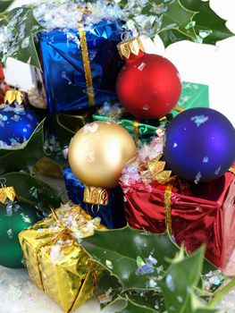 Colorful gift boxes, Christmas bulbs and holly, sprinkled with artificial snow. Isolated on a white background.