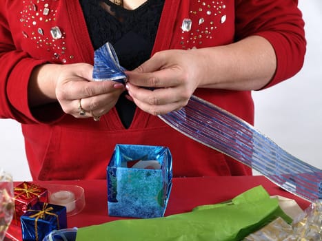 A woman forms a blue bow out of a shiny ribbon as she wraps a present.