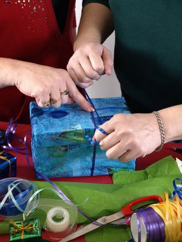 Two people wrapping colorful presents, helping each other tie a knot with ribbon.