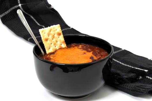 Bowl of chili with melted cheese, cracker, spoon, and scarf.  Isolated on white background.