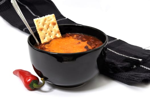 Bowl of chili with melted cheese, cracker, red cayenne pepper, spoon, and scarf.  Isolated on white background.