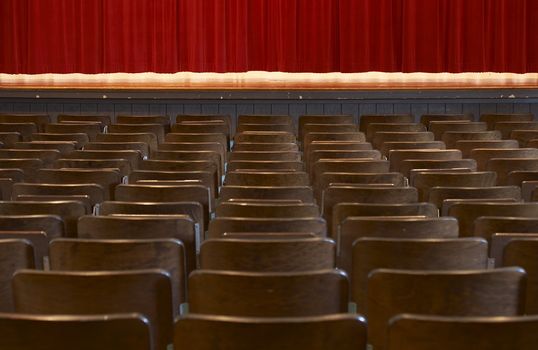 rows of wood chairs in an old auditorium and a red curtain