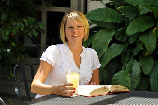 Blond female student studying with textbook and glass of lemonade. 