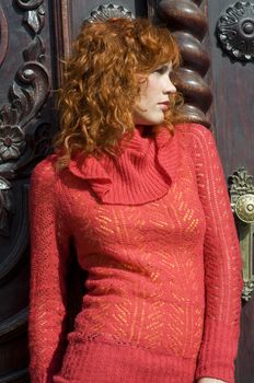 close up of a young and beautiful woman with red pullover near old door