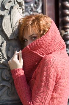 red haired woman hidding herself behind her red pollover near old building