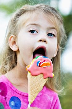 Little girl licking a sucker that is in the shape of an ice cream cone.