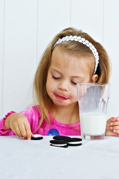 Little girl eating creme filled cookies while drinking a glass of milk. 