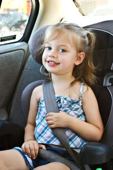 Little girl in a car seat smiles at viewer.