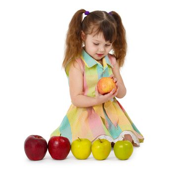 The little girl sits on a white background with apples