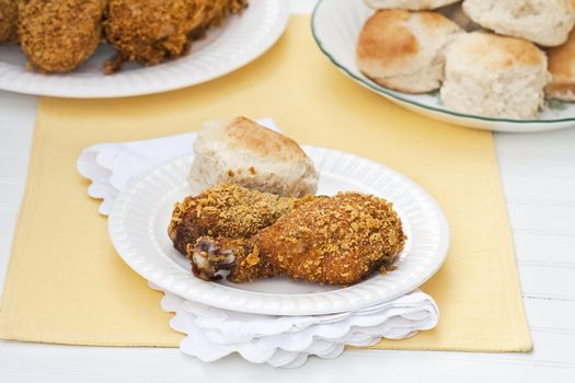 Oven fried skinless chicken with fluffy homemade biscuits on a rustic white table. Shallow DOF with selective focus on the chicken in front.