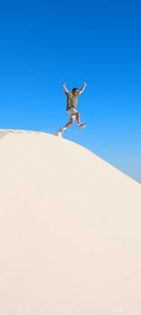 An image of a man jumping off a sand dune