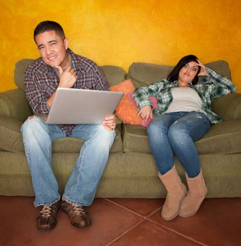 Bored Hispanic woman reacting to man with computer on green couch