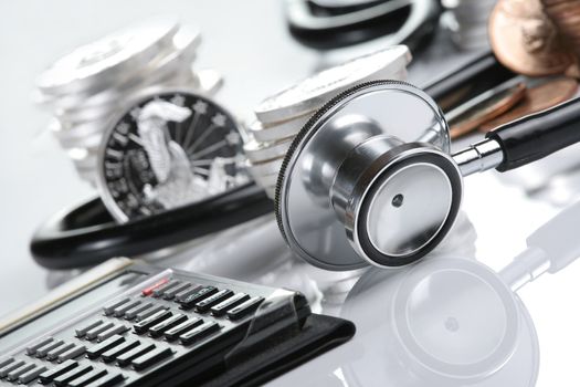 Financial health concept, stethoscope weaving around stacks of silver and gold coins and calculator