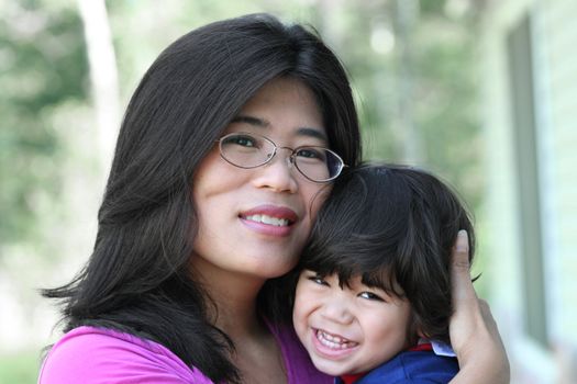 Asian mother lovingly holding her son outdoors in summer