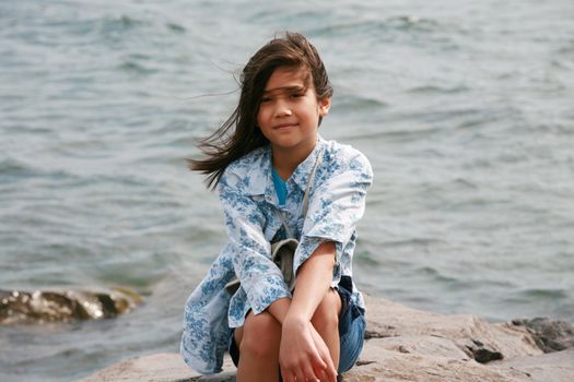 Nine year old girl sitting by lake in summer. Part asian- Scandinavian background.