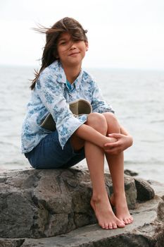 Nine year old girl sitting by lake in summer. Part asian- Scandinavian background.