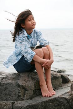 Nine year old girl sitting by lake in summer. Part asian- Scandinavian background.