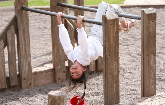 Little girl hanging upside down on parallel bars at playground