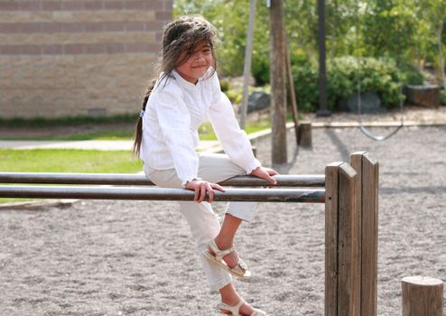 Little girl sitting on top of parallel bars at playground