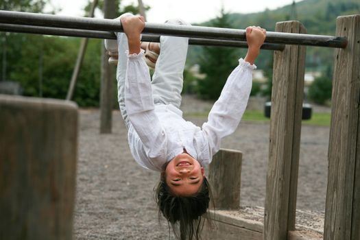 Little girl hanging upside down on parallel bars at playground