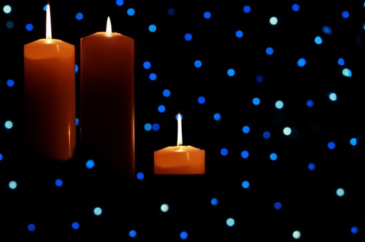 Three burning candles with blue lights in background, dark shadows