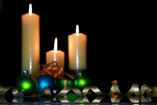 Three burning candles with Christmas ornaments, dark shadows