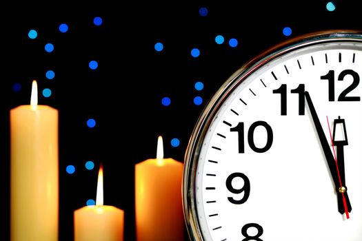 Clock set at three minutes to midnight with blue Christmas lights in background and candles burning