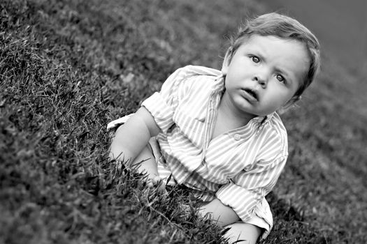 Cute young baby sitting in the grass in black and white.