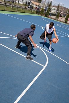 A young basketball player guards his opponent during a one on one basketball game at the park.