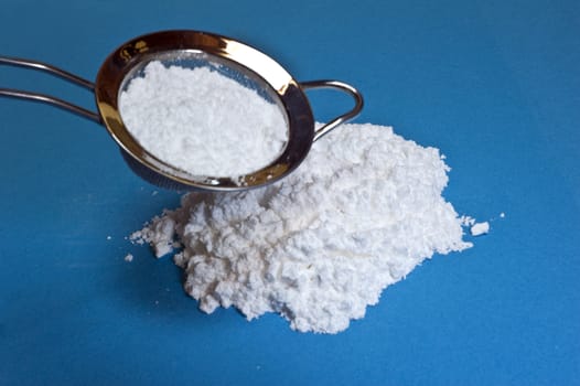 Icing sugar and sieve on a blue background