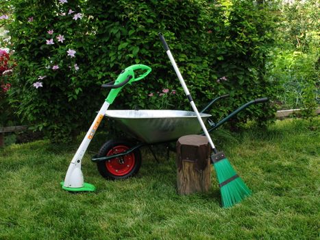 Wheelbarrow broom and grasstrimmer on green grass in garden
