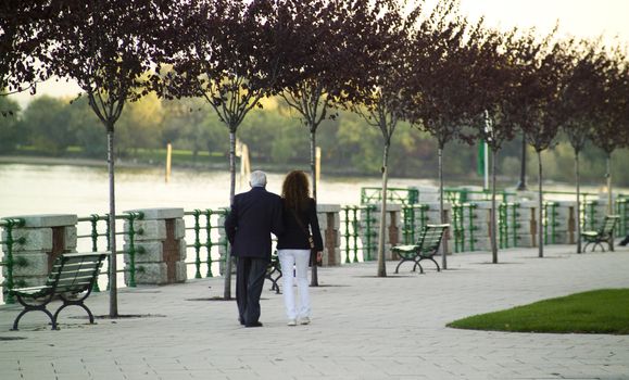 an old mand and a young woman walking by the lake