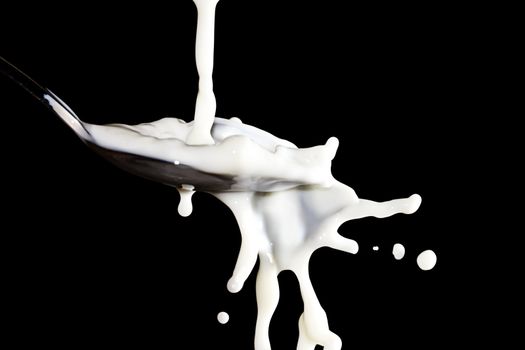 some milk flows over a spoon with black background