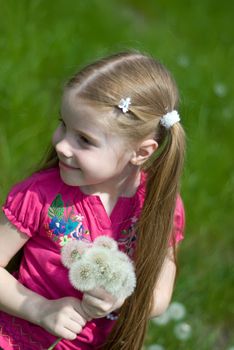 smiling little girl on a green meadow with a bouquet of dandelions