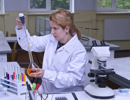 Image of a female researcher dropping a solution into a recipient in a laboratory.