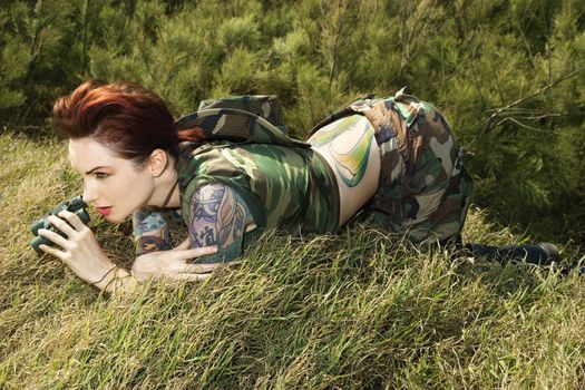 Attractive tattooed Caucasianwoman in camouflage lying on grass looking through binoculars in Maui, Hawaii, USA.