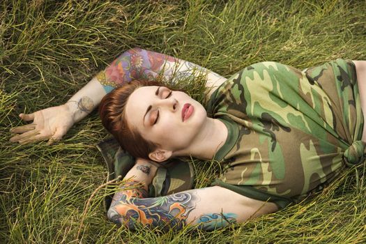 Attractive tattooed Caucasian woman in camouflage lying on grass in Maui, Hawaii, USA.