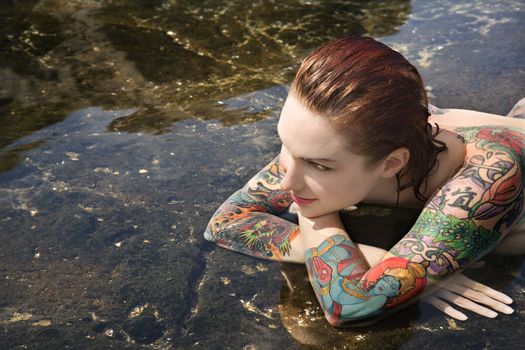 Sexy nude tattooed Caucasian woman lying in tidal pool in Maui, Hawaii, USA.