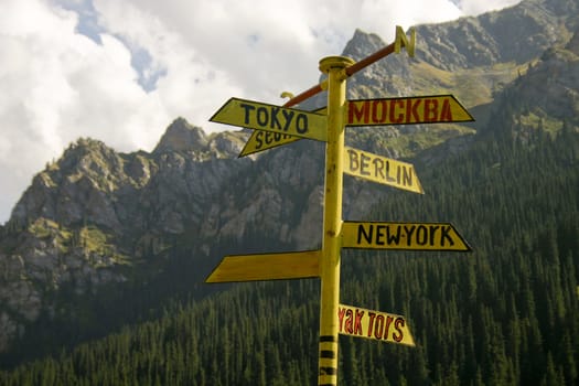 The signpost from meta indicating a managements seven large cities of the world, on a background of mountains.