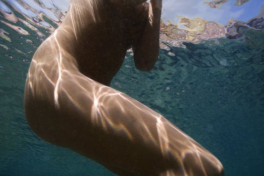 Underwater view of young Asian nude female torso and legs.
