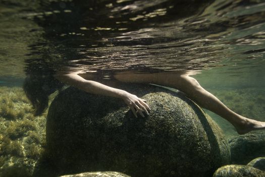 Caucasian young nude woman partially submerged underwater lying on back on rock.