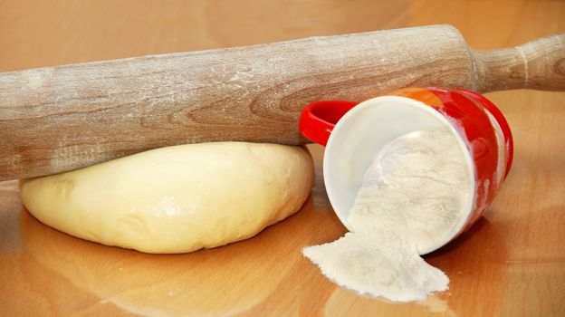rolling pin over dough and cup with flour on table in kitchen