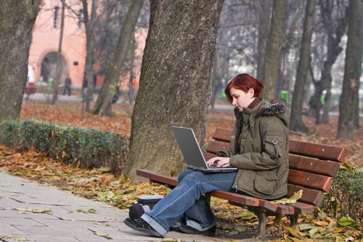 Redheaded young woman working on a laptop in a park in autumn.