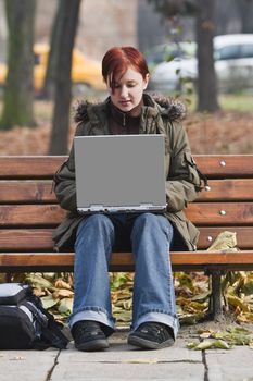 Young redheaded girl working on a laptop in an autumn park.