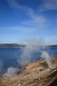Blue lake waters with steam rising from hot springs in foreground