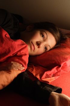 Beautiful female lying in bed trying to fall asleep.  Image for insomnia, sleeplessness, stress, sadness, etc.  Lit by a night light beside the bed.
