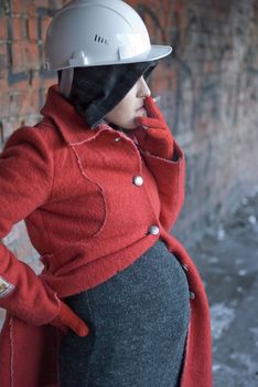 Pregnant woman in red coat and helmet smokes a cigarette