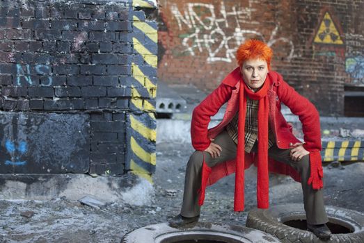 Red-haired woman stands on the old tires in active and strong pose. She is stright looking to the camera