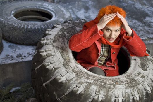 Red-haired woman feels safe and shows the symbol of safety (home). She is sitting in the old tire